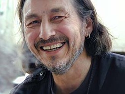 John Trudell is an acclaimed poet, national recording artist, actor and activist whose international following reflects the universal language of his words, work and message. Trudell (Santee Sioux) was a spokesperson for the Indian of All Tribes occupation of Alcatraz Island from 1969 to 1971. He then worked with the American Indian Movement (AIM), serving as Chairman of AIM from 1973 to 1979. In February of 1979, a fire of unknown origin killed Trudell’s wife, three children and mother-in-law. It was through this horrific tragedy that Trudell began to find his voice as an artist and poet, writing, in his words, “to stay connected to this reality.” 