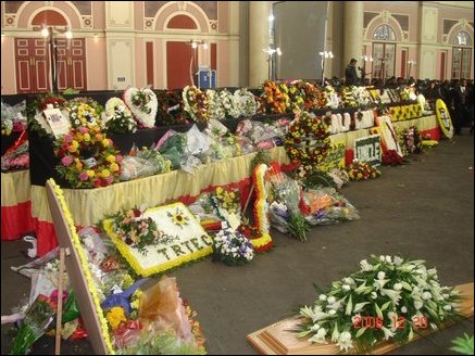 Dozens of wreaths and bouquets are being placed alongside the casket by mourners as they pass.